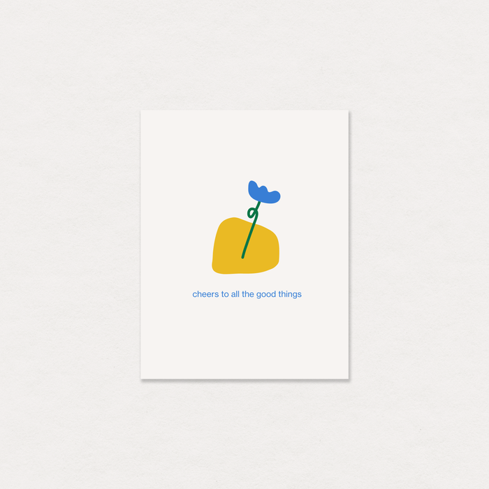 A minimalist art print greeting card featuring a yellow abstract shape with a blue flower and green stem, and the text 'cheers to all the good things' below, displayed on a textured off-white background.