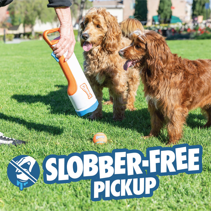 Someone uses the Chuckit! Cannon & Cannon Max Dog Ball Launcher by Chuckit! to pick up a tennis ball in front of two long-haired brown dogs on green grass. Text reads Slobber-Free Pickup with a no slobber icon.