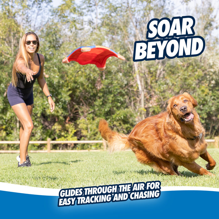 A woman throws the Chuckit! Flying Squirrel by Chuckit!—a durable red fetch toy—for her golden retriever, who chases it across sunny park grass. Text: “SOAR BEYOND” and “Glides through the air for easy tracking and chasing.”.