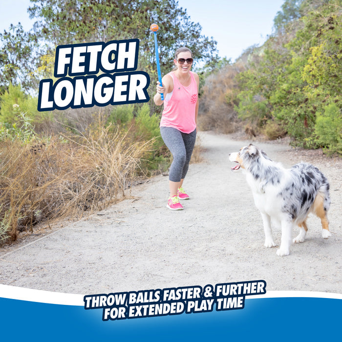A woman in athletic wear uses the Chuckit! Junior 18M Dog Ball Launcher for hands-free fetch with her energetic dog on a wooded dirt trail. Text: FETCH LONGER – Throw balls faster & further with Chuckit! for more playtime.
