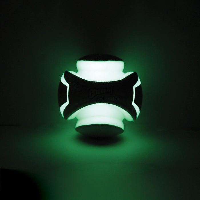 The Chuckit! Kick Fetch Max Glow by Chuckit! glows with a bright green light in the dark, showcasing its distinct geometric design and textured surface.