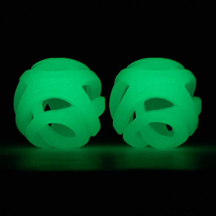 Two round, hollow, green Chuckit! Max Glow Air Fetch Balls with interwoven bands glow brightly in the dark against a black background.