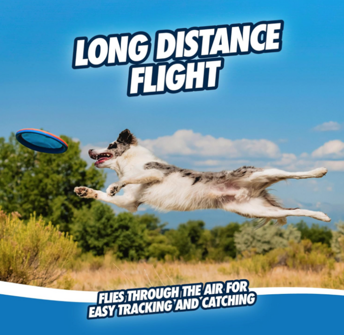 A white and brown dog leaps to catch a Chuckit! Paraflight Max Glow Flyer Dog Toy, with green bushes and a partly cloudy sky behind. Text: Chuckit! Long distance flight—flies through the air for easy tracking and catching.