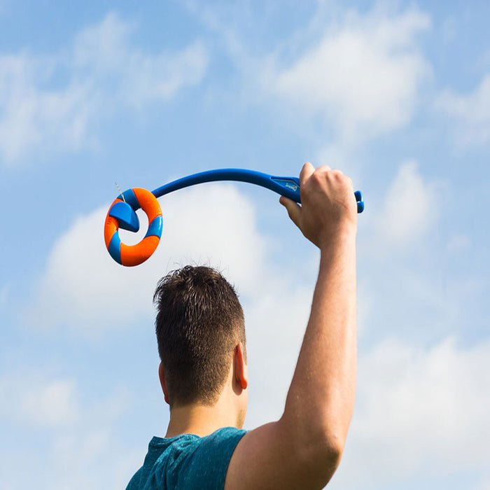 A person seen from behind holds up a Chuckit! RingChaser Dog Toy Set by Chuckit! with its orange and blue ball against a partly cloudy sky.
