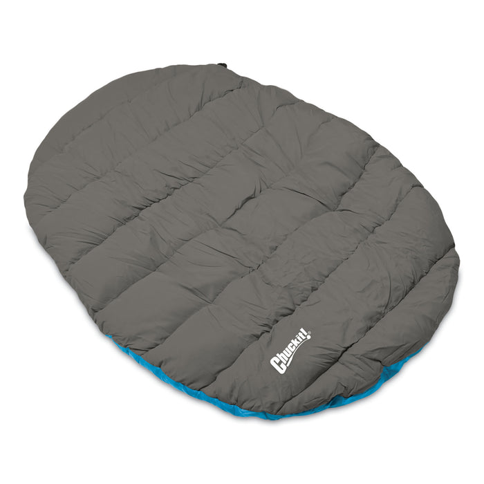 The Chuckit! Travel Pillow Bed is a large, oval, gray quilted sleeping bag with a blue lining and the Chuckit! logo in white on the bottom right—a perfect portable dog bed for adventures.