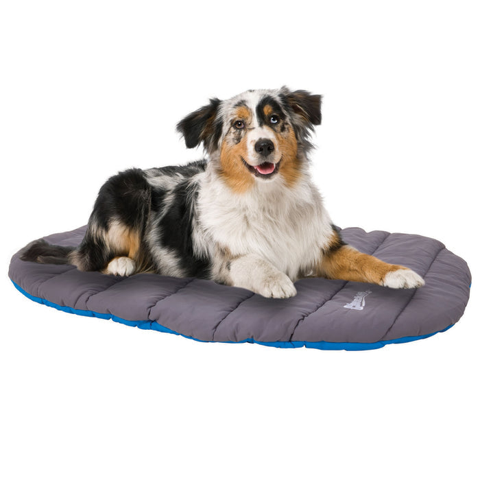 An Australian Shepherd relaxes on a gray and blue Chuckit! Travel Pillow Bed by Chuckit!, looking ahead with its mouth open and tongue out, enjoying the comfort of this portable dog bed.
