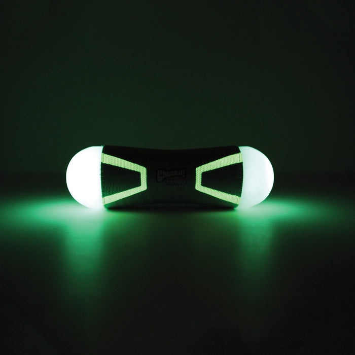 The Chuckit! Tumble Bumper Max Glow is a black dog fetch toy with rounded ends that emits a soft green glow, lighting up dark surfaces. The product features the Chuckit! name faintly visible at its center.