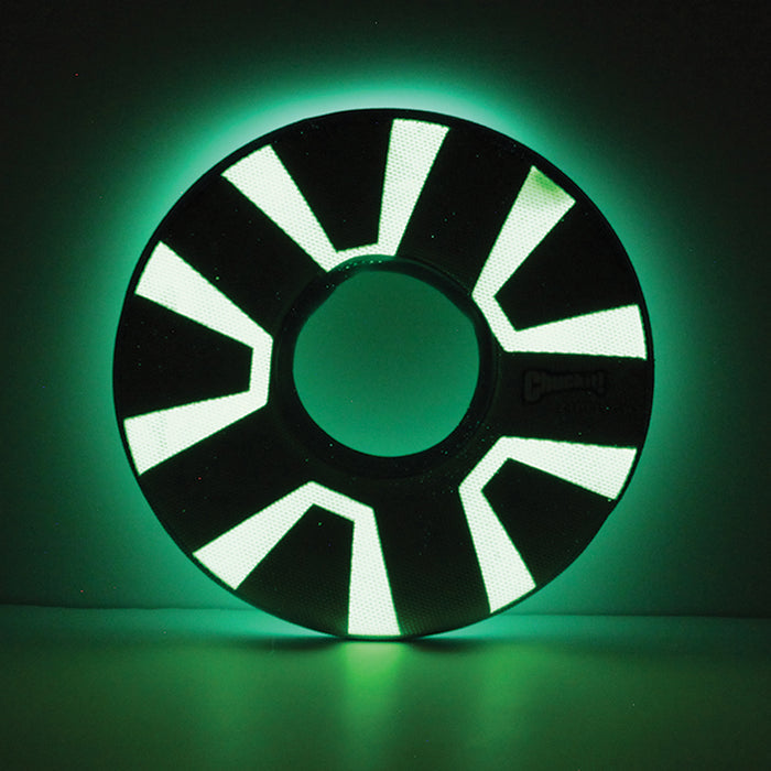 The Chuckit! Zipflight Max Glow Dog Toy by Chuckit! is a black, circular toy with a hollow center and bright green geometric patterns that glow in the dark, making it easy to spot against dark backgrounds.