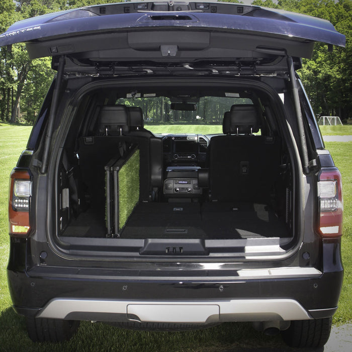 The open trunk of an SUV parked on grass shows one back seat folded down and a Gen7 Natural-Step® Ramp for Vehicles stored in the cargo area, with trees and a soccer goal visible in the background.