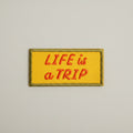 Rectangular shaped iron-on patch with a yellow background and red words that say "Life is a trip".