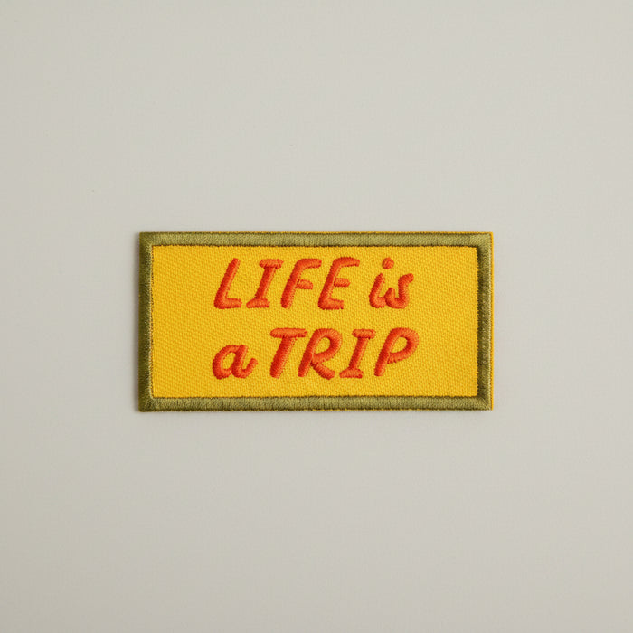 Rectangular shaped iron-on patch with a yellow background and red words that say "Life is a trip".