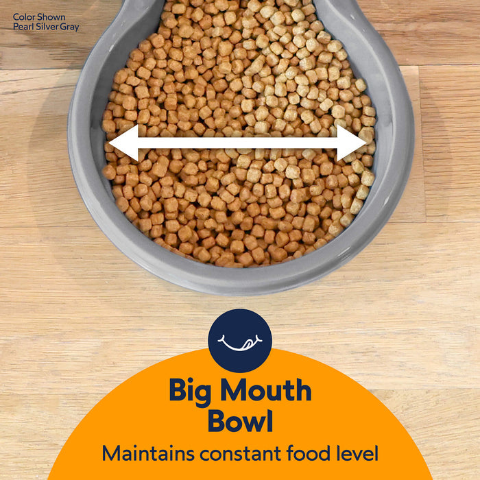 A gray Petmate Replendish Pet Feeder With Microban is shown from above, filled with kibble. A white double-headed arrow highlights its wide opening. Text: Petmate – gravity feeder maintains a constant food level.