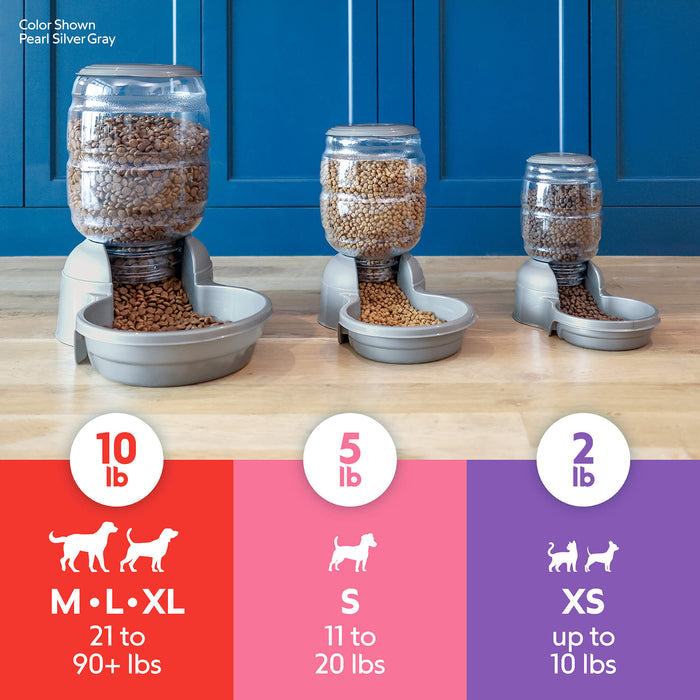 Three Petmate Replendish Pet Feeders with Microban are shown on a wood floor against a blue wall. Each automatic feeder is labeled: 2 lb for XS, 5 lb for S, and 10 lb for M, L, XL. All feeders are filled with kibble.