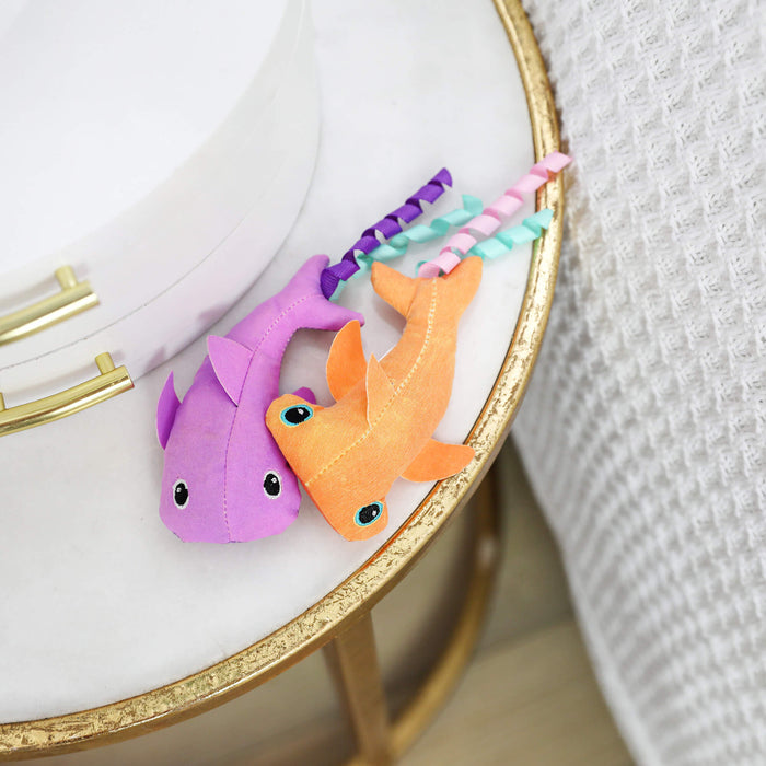 The Quirky Kitty Color Changing Shark 2pk—ocean-themed catnip toys—features two vibrant shark designs on a white and gold table, making them perfect interactive toys for playful felines.