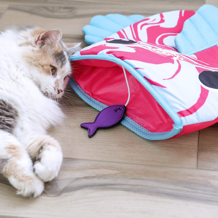 A fluffy cat lounges on a wooden floor near the Quirky Kitty Fish Cooling Mat—an ocean-themed play mat—next to a colorful tunnel with a dangling purple fish toy, creating endless fun for your playful feline.