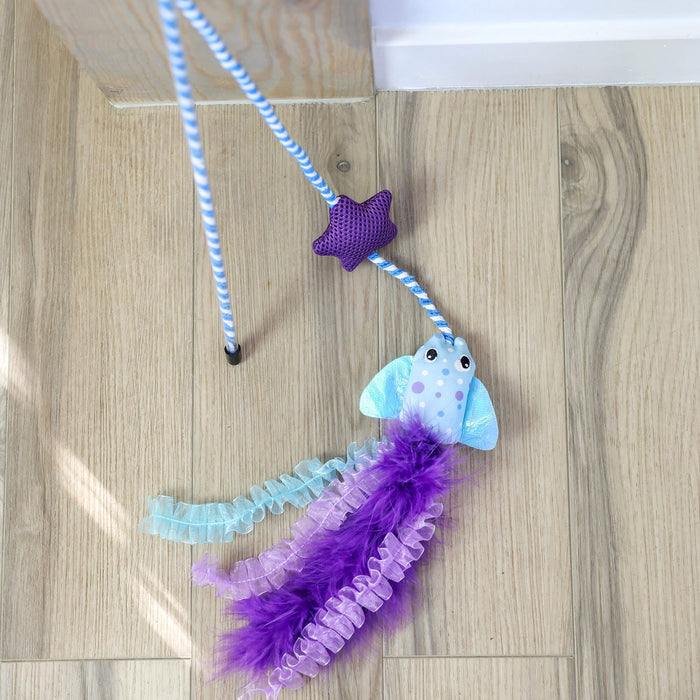The Quirky Kitty Manta Ray Wand – Interactive Cat Wand Toy with Catnip features a blue and white striped handle, a purple star, and a blue fish with ribbons and feathers, resting on a light wooden floor.
