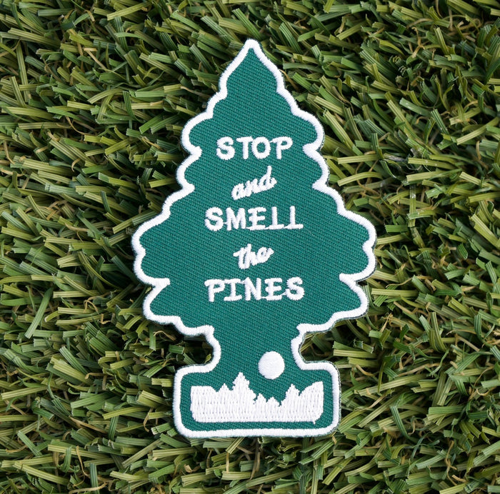 Iron-on embroidered patch with the shape of a pine tree and the words "Stop and smell the pines".
