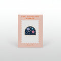 Enamel pin with planets and stars, in a black background, and the words "Space Cadet" in gold.